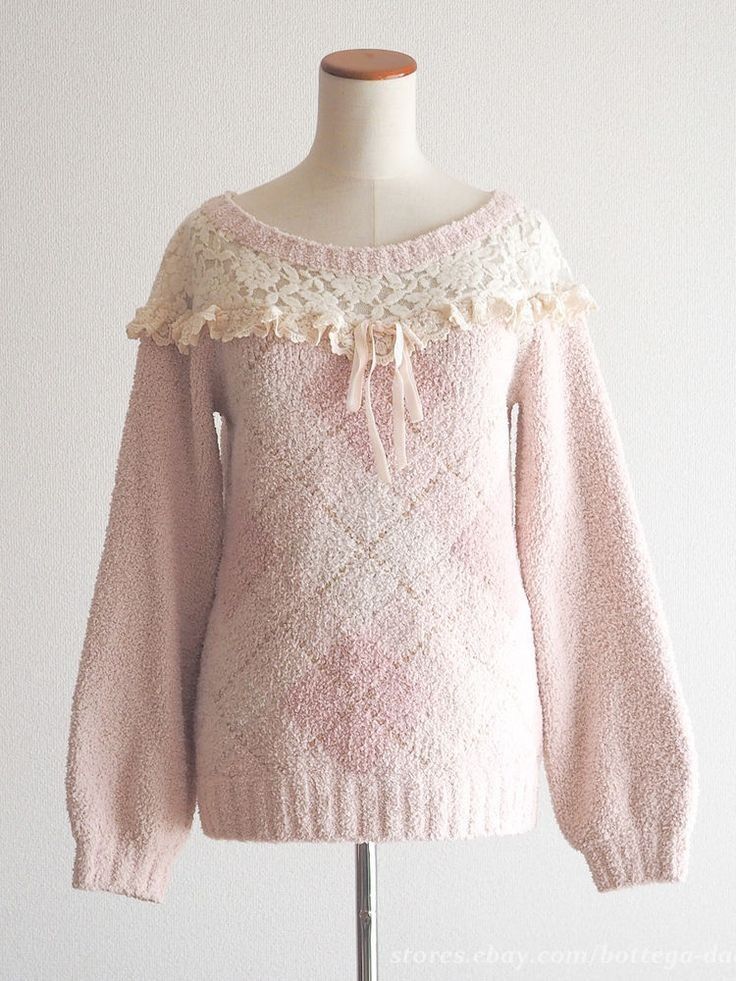 a light pink knit sweater with a delicate white lace collar and a ribbon tie is displayed on a mannequin against a plain background. the sweater features a subtle chevron pattern in shades of pink and white, adding a touch of texture. the soft lighting and neutral background enhance the romantic and feminine aesthetic of the garment.