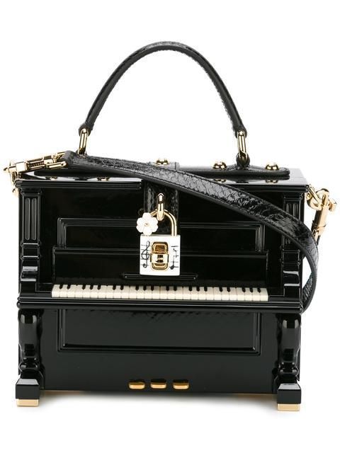 black piano shaped handbag with gold accents and a small white flower on the side. the bag has a top handle and a detachable shoulder strap.