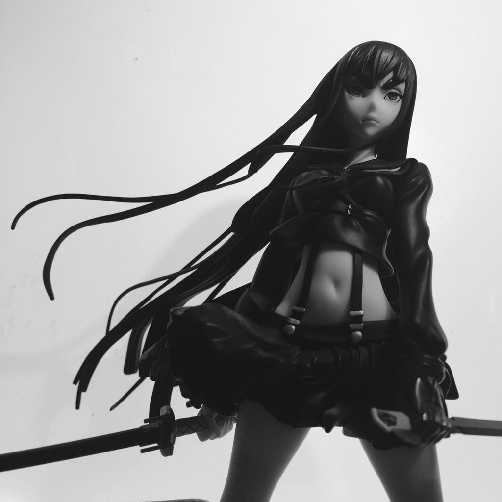 a black and white image of a black rock shooter figurine. she is in a dynamic pose, holding her sword with both hands and her long black hair flowing behind her. the low angle shot adds to the sense of action and power.  the image has a strong contrast with deep shadows and highlights.
