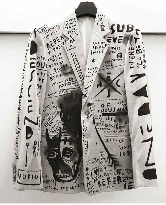 a blazer with graffitistyle art and text covering it is hanging on a hanger. the style resembles the art of jeanmichel basquiat.