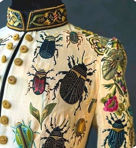 a closeup shot of a jacket with detailed embroidery. the jacket is decorated with various beetle designs, floral patterns, and intricate collar and button details.