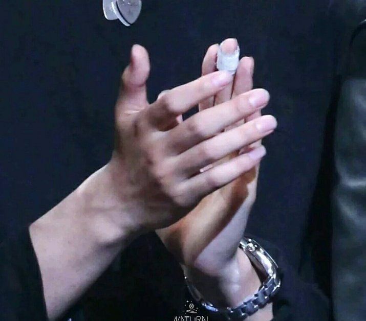 a closeup image of a person's hands. one hand is slightly raised, and the person is wearing a watch on their other wrist. the photo appears to have been taken indoors in dim lighting.