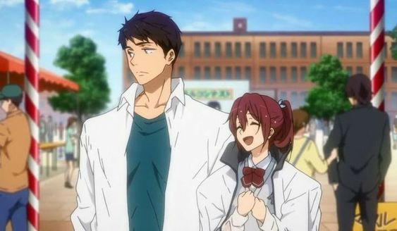 he image shows a young man and woman, drawn in an anime style, standing together on a city street. the man is tall with dark hair and a white shirt, while the woman is shorter with long reddishbrown hair and a school uniform. they appear to be at a festival, as indicated by the colorful banners and crowds in the background. the overall atmosphere is bright and cheerful.
