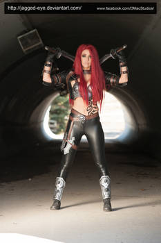 the image showcases a female cosplayer portraying riven from the popular video game league of legends.  she's dressed in meticulously crafted armor and clothing that closely resembles riven's ingame appearance. the cosplayer has long, vibrant red hair and is wielding two swords. the setting is a dark tunnel, providing a dramatic backdrop that enhances the overall effect of the powerful pose.  the image is professionally lit and photographed, capturing the detail of the costume and the intensity of the character's expression.