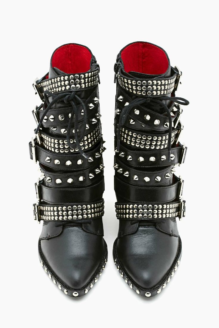 a closeup studio shot shows a pair of women's black leather ankle boots. the boots feature multiple silverstudded buckles, pointed toes, and a red interior lining.  they are styled in a rock and roll or punk aesthetic. the boots are positioned on a white background, showing both the front and side profiles clearly.