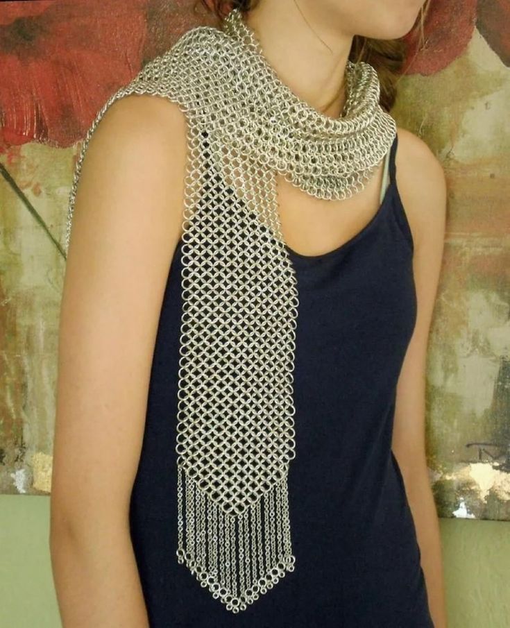 a woman wearing a chainmail scarf. the scarf is silver in color and has a fringe on the bottom. the woman is wearing a blue tank top. the background is blurred.