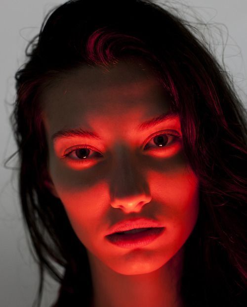 a closeup portrait of a young woman with dark hair, her face illuminated by intense red light. the lighting emphasizes her features, creating dramatic shadows and conveying a sense of mystery and emotion. her eyes are dark and piercing, and her expression is somewhat somber.