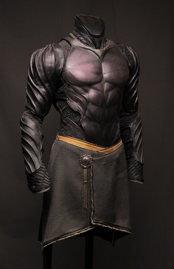 a closeup shot of a man wearing intricate black leather armor, with a dark fabric skirt. the armor is detailed and has a futuristic look to it. the image is shot against a dark background.
