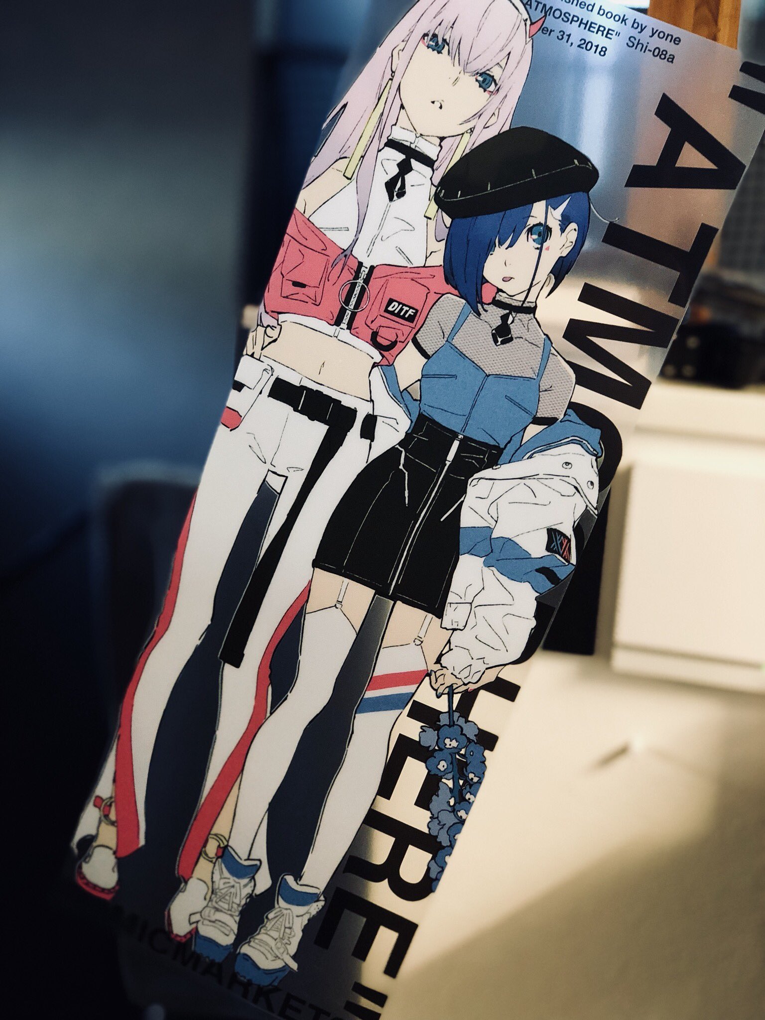 a clear acrylic bookmark featuring an illustration of two anime girls with pink and blue hair, dressed in trendy streetwear. the bookmark is titled "atmosphere" and has a publication date of "yer 31, 2018".