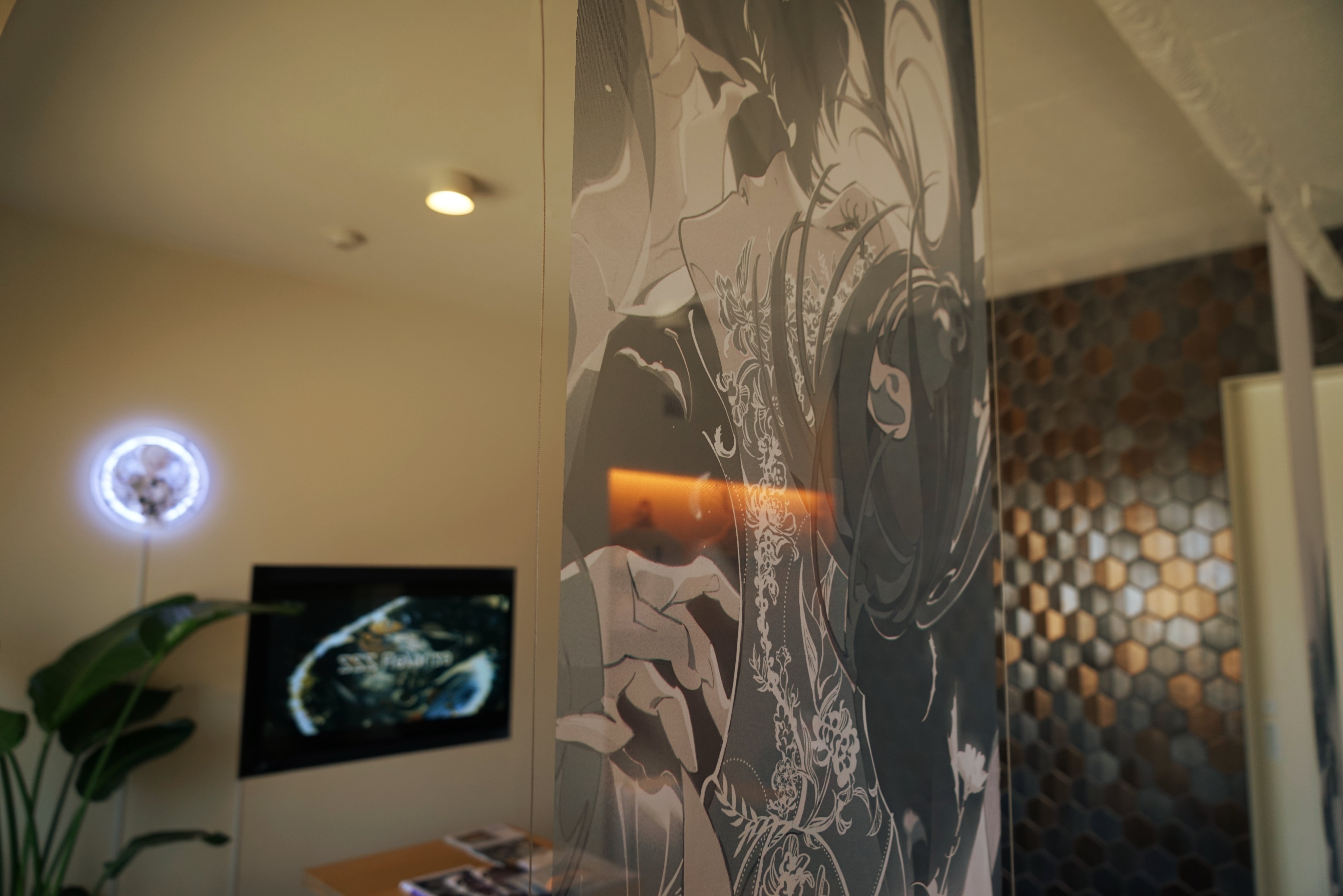 this image shows the interior of a home or office with a modern aesthetic. the focus is an artwork printed on clear acrylic depicting a person with elaborate tattoos. the artwork partially obscures the background, which features a television, a plant, and a tiled wall. the room is welllit, likely by natural light.