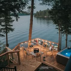 the image shows a beautiful lake house deck at dusk. the deck is made of wood and features a fire pit in the center, surrounded by comfortable outdoor furniture. there is also a hot tub on the deck, providing a relaxing spot to enjoy the view. the lake is calm and serene, surrounded by lush green trees. the scene is illuminated by soft lighting, creating a warm and inviting atmosphere. the overall aesthetic is luxurious and tranquil, perfect for a relaxing vacation.