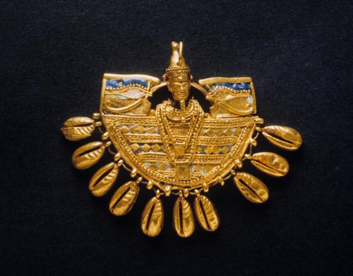 a golden ornament in the shape of a half circle with a figure of an egyptian pharaoh with a blue and white headdress is in the center, and the outer edge is lined with teardropshaped drops.