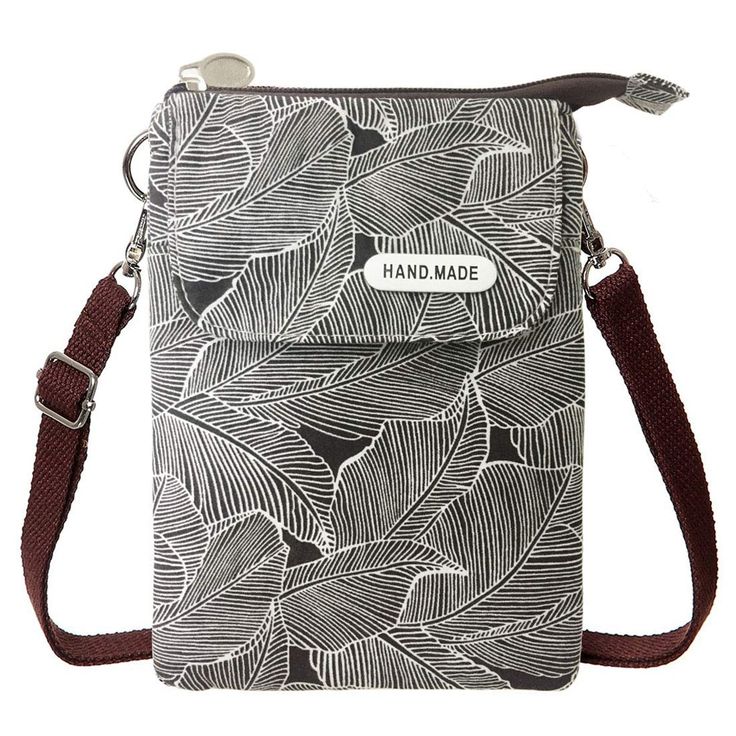 a fabric crossbody bag with a black and white leaf pattern and a brown adjustable strap. the bag has a flap with a "hand.made" tag on it. it also has a zipper at the top and metal hardware.