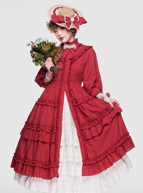 a woman poses in a studio setting wearing a red lolita fashion dress with white lace trim and a full skirt. she holds a bouquet of flowers in one hand and wears a straw hat adorned with a bow. the background is plain white, and the lighting is soft, highlighting the details of the outfit.