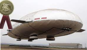 a large blimp or airship is shown in the sky. the airship is white and gray in color and has the words "dream dream" on the side of the fuselage. the airship is in flight and the ground can be seen in the background.