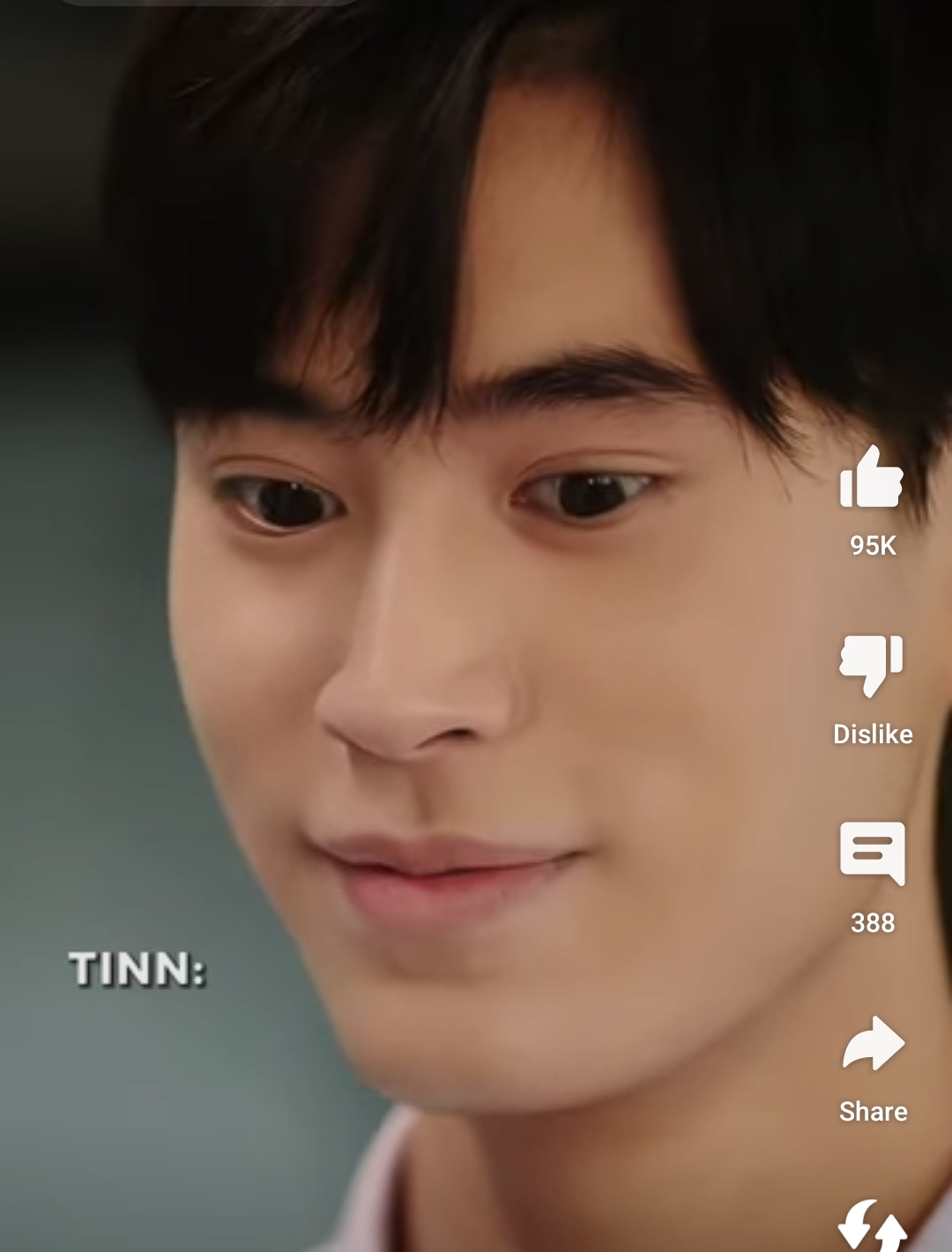 the image is a closeup shot of a young asian man with short black hair and brown eyes.  he is smiling slightly and his expression is warm and inviting. the lighting is soft and diffused, giving his skin a healthy glow. he appears to be indoors.  there are social media engagement icons visible on the right side of the image, suggesting it is a screenshot from a video or social media platform.  the name "tinn" is visible in the bottom left corner.