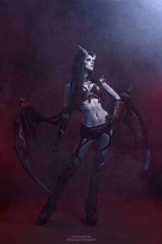 a striking cosplay photograph of a female demon or succubus. the model is posing dramatically against a dark red and blue smoky background. she's wearing elaborate makeup and a costume with horns, wings, and armorlike details. the overall aesthetic is dark, gothic, and fantasyinspired, with strong use of dramatic lighting to enhance the mood and atmosphere. the model's pose and expression add to the mysterious and powerful feel of the image. the weapon/prop she carries completes the overall look.