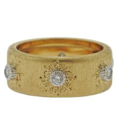 a closeup of a gold band ring with diamonds set in intricate designs around the ring. the ring has a brushed gold finish and a classic style. it's perfect for a wedding or engagement.