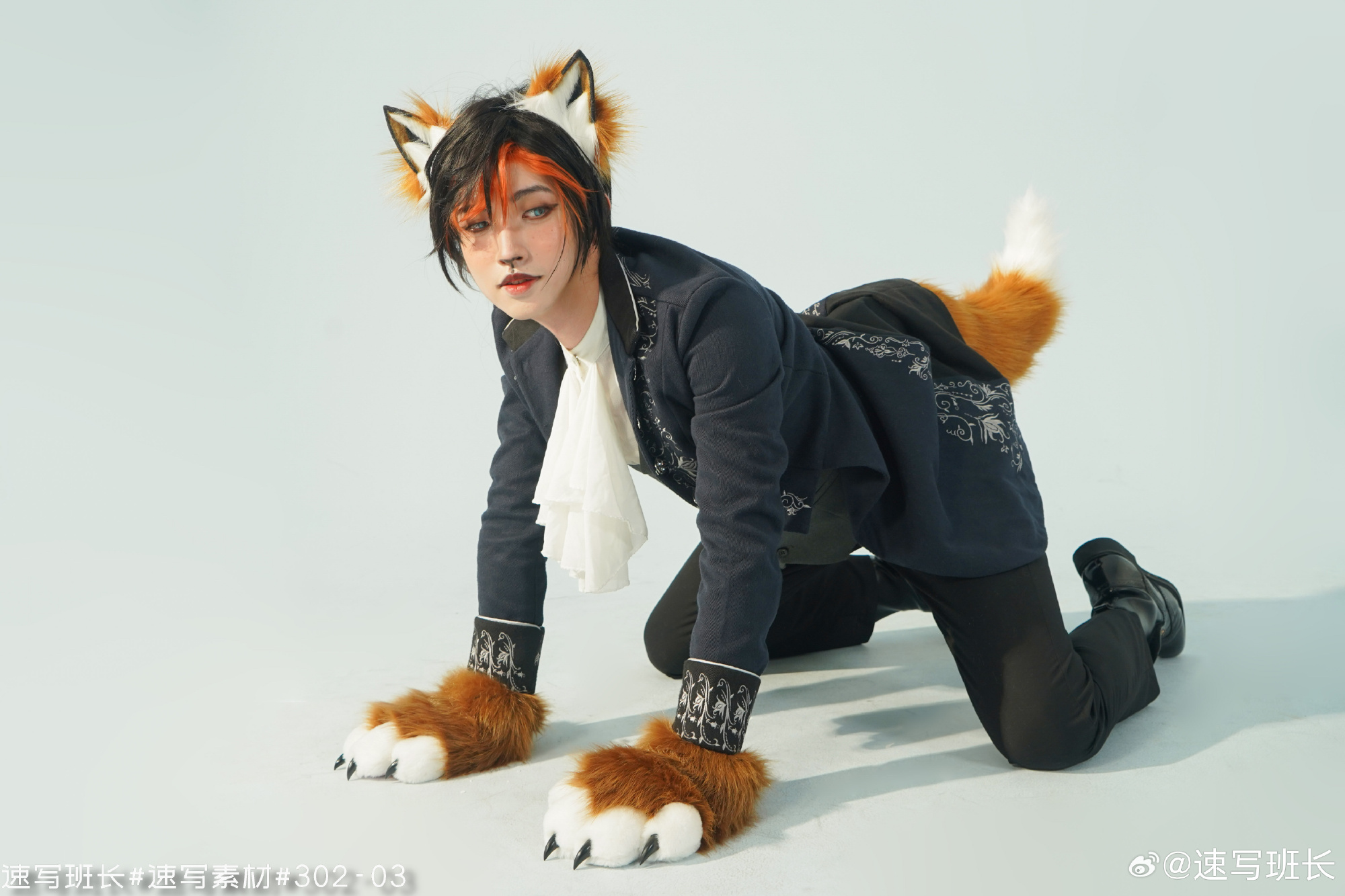 a man in a fox costume is posing on all fours against a white background. he's wearing a blue jacket, black pants, black boots, and white gloves. he has fox ears, a fox tail, and makeup to look like a fox.