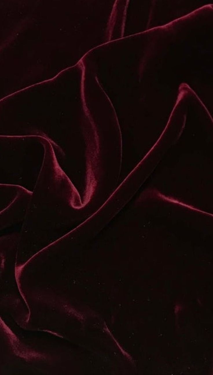 a closeup shot of luxurious, deep maroon velvet fabric, showing intricate folds and drapes. the image emphasizes the fabric's soft, rich texture and smooth sheen.