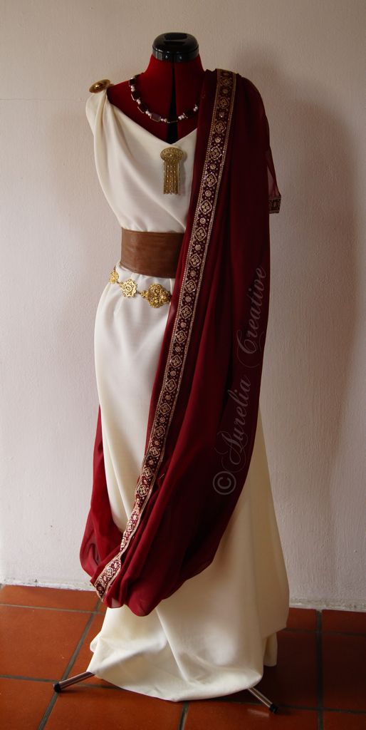 he image shows a mannequin dressed in a meticulously recreated romanstyle women's garment. the outfit consists of a creamywhite stola (a long, loosefitting tunic), cinched at the waist with a brown leather belt adorned with gold embellishments.  a deep burgundy palla (shawl or overdress) is draped over the stola, featuring gold detailing along one edge.  gold jewelry, including a necklace and a pendant, completes the look. the dress is displayed on a mannequin against a white wall and terracottatiled floor. the overall impression is one of historical accuracy and elegance.