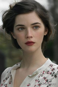 this is a closeup portrait of a young woman with brown hair and eyes. she is wearing a white floral blouse and has a natural makeup look. the lighting is soft and natural, and the background is blurred, creating a dreamy and romantic feel.