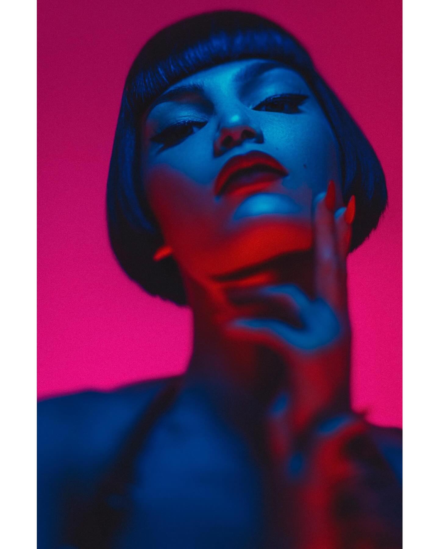 the image is a stylized closeup portrait of a woman with a blunt bob haircut.  she's looking slightly upwards. the lighting is dramatic, using strong contrasting colors of magenta (pinkred) and cyan (bluegreen), which creates a highcontrast, almost neon effect. the woman's face and neck are sharply lit while the rest of her body fades slightly into shadow. her expression is serious and sensual, hinting at a powerful and glamorous persona. the overall aesthetic has a retro or vintage feel, possibly inspired by the 1920s flapper style.