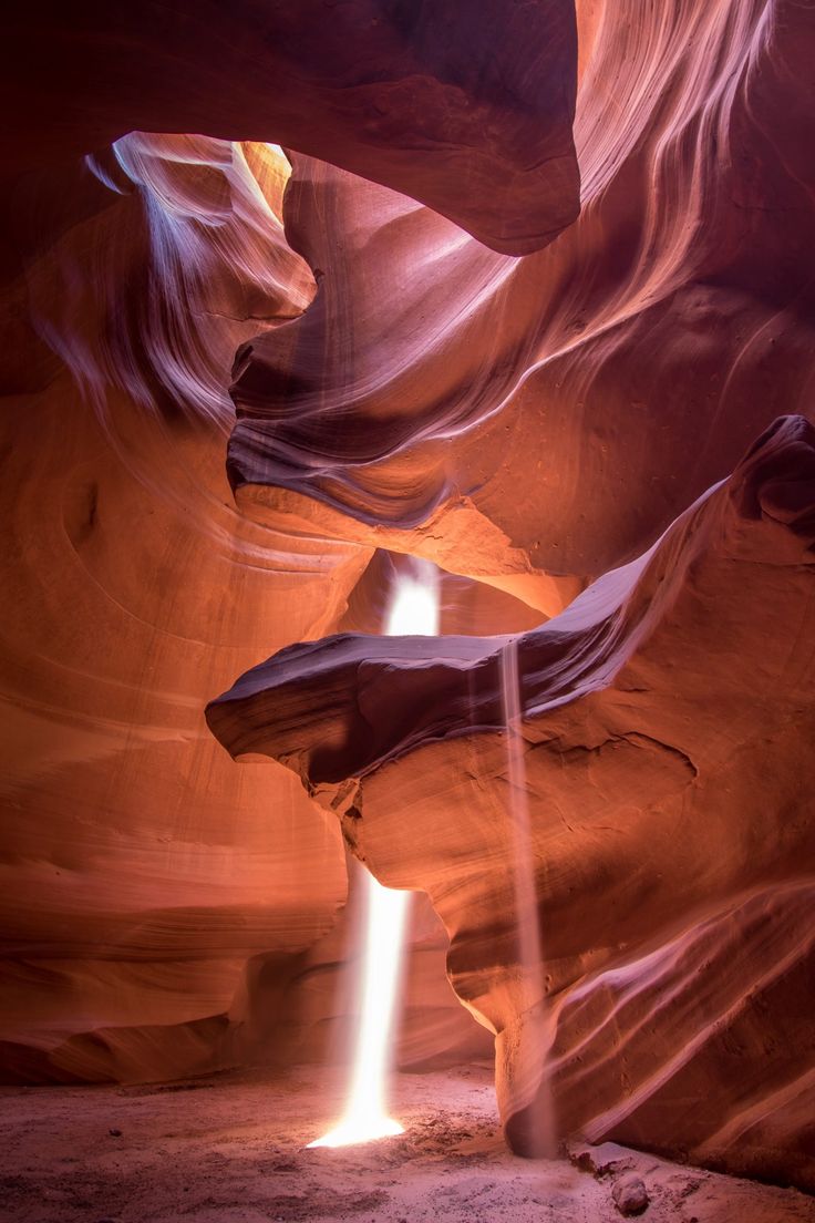 a low angle view of a narrow slot canyon with light streaming in from the top of the canyon. the sandstone walls of the canyon are orange and red and are carved into interesting shapes.