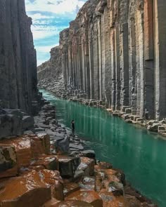 a stunning view of a basalt canyon in iceland. the basalt columns form a natural wall on either side of the river, which flows through the canyon. the water is a vibrant green, reflecting the sunlight. the rock formations are both rugged and beautiful, creating a unique and aweinspiring landscape.