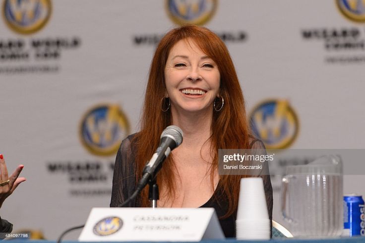 a woman with long, red hair is smiling and speaking into a microphone at a conference event. she's dressed in a black shirt and looks very casual and comfortable. she's talking to a large crowd of people and is looking directly at the camera. she has light skin and is a caucasian woman. the photo is a closeup portrait.