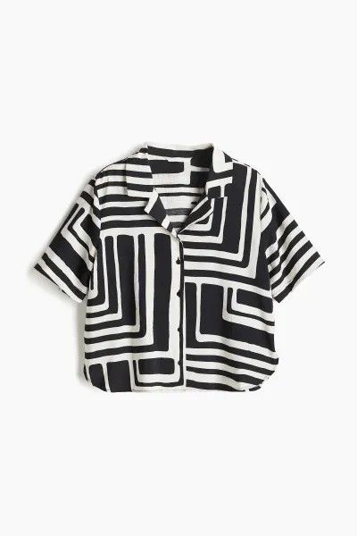 a black and white patterned shortsleeved shirt is displayed on a white background. the shirt has a buttondown front and an abstract design featuring geometric shapes.