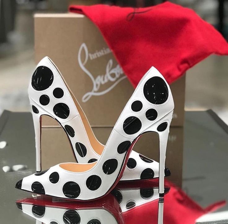 a pair of white polka dot christian louboutin high heels with red soles. the shoes are sitting on a white surface with a red bag in the background. the shoes are brand new and look very expensive. they are a popular style of shoe that is worn by many women. they would make a great addition to any wardrobe.
