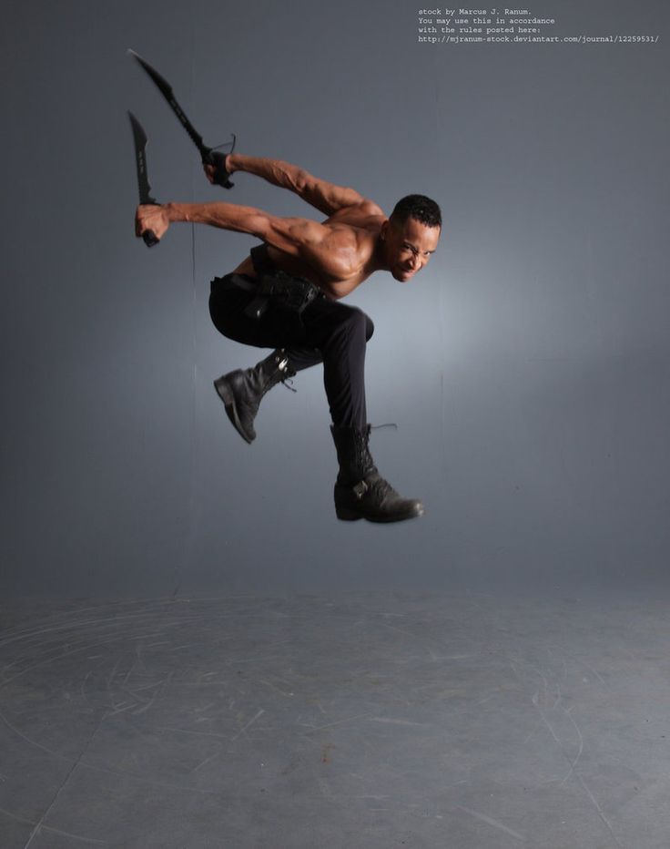 a shirtless man jumps through the air, holding two swords in his hands. he is midjump and looking intently at the camera. his muscles are defined and he is posed in a dynamic, actionpacked pose.  he is in a studio setting, in front of a grey background. the image has a dark, dramatic feel.