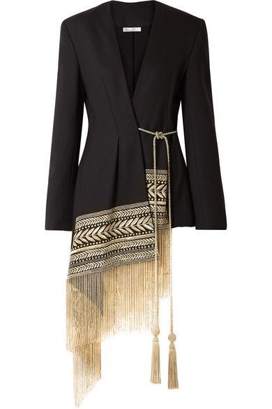a black blazer with a deep vneck and a long, angled fringe attached to one side. the fringe has an aztec pattern along the top, followed by long gold tassels. there is a tie at the waist.