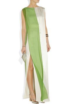 a woman in a white and green sleeveless dress is standing in a studio. she is wearing gold high heels and holding a silver clutch. the background is white.