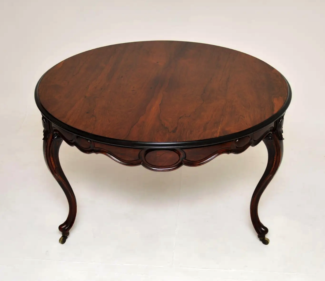 a closeup shot of an antique, round, mahogany table. the table has carved legs and an ornate design around the edge. the table is made of dark wood and is in good condition.