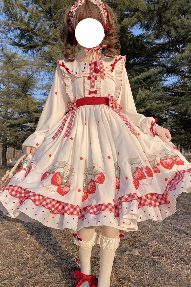 a woman wearing a strawberrythemed lolita dress stands in a park. the dress is white with red and green strawberry print and red gingham trim. the woman is posing with her arms outstretched, showing off the full skirt of the dress. the lighting is bright and natural, and the overall aesthetic is playful and feminine.