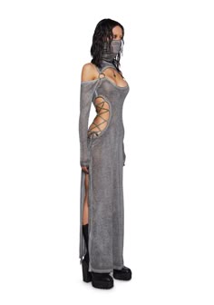 a woman wearing a long, grey, knit dress with high slits on the sides. she is wearing black high heels, and her look is completed with a black face mask.