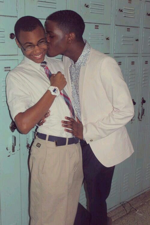 two teenage boys in a school locker room, they are standing close together, and one has his arm around the other's shoulder, while the other one has his arm around the other's waist, they are both smiling and appear to be very close.