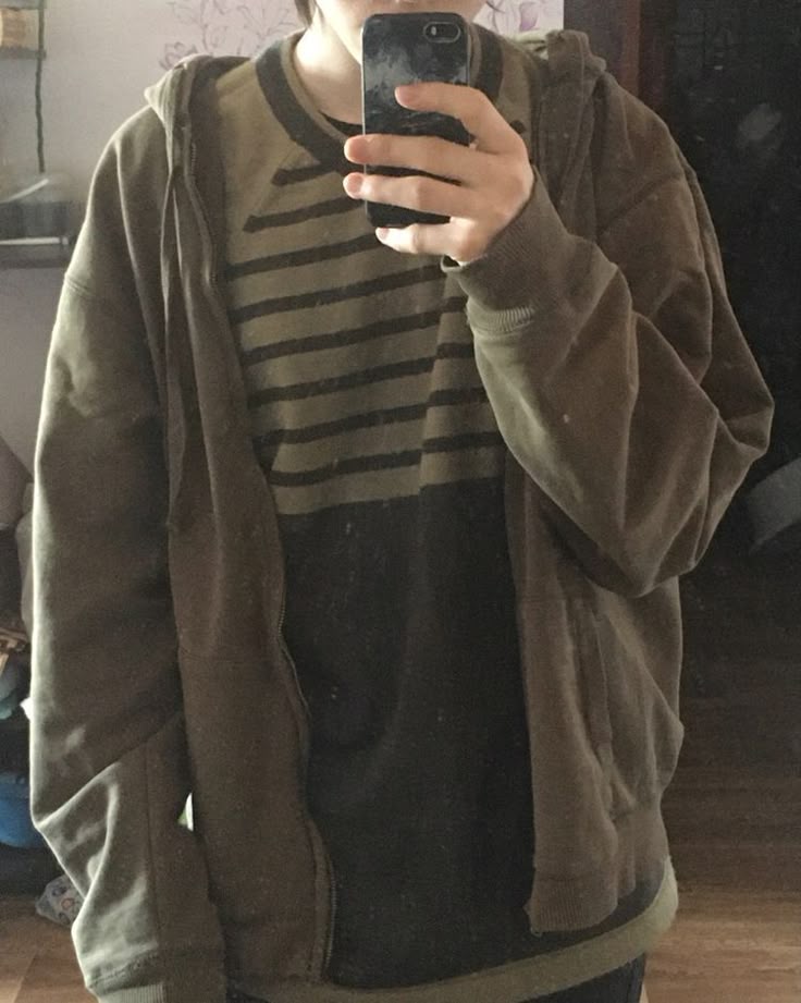a person is taking a selfie in a mirror. the person is wearing a striped shirt and a zippedup hoodie. the hoodie is green and has a front pocket.