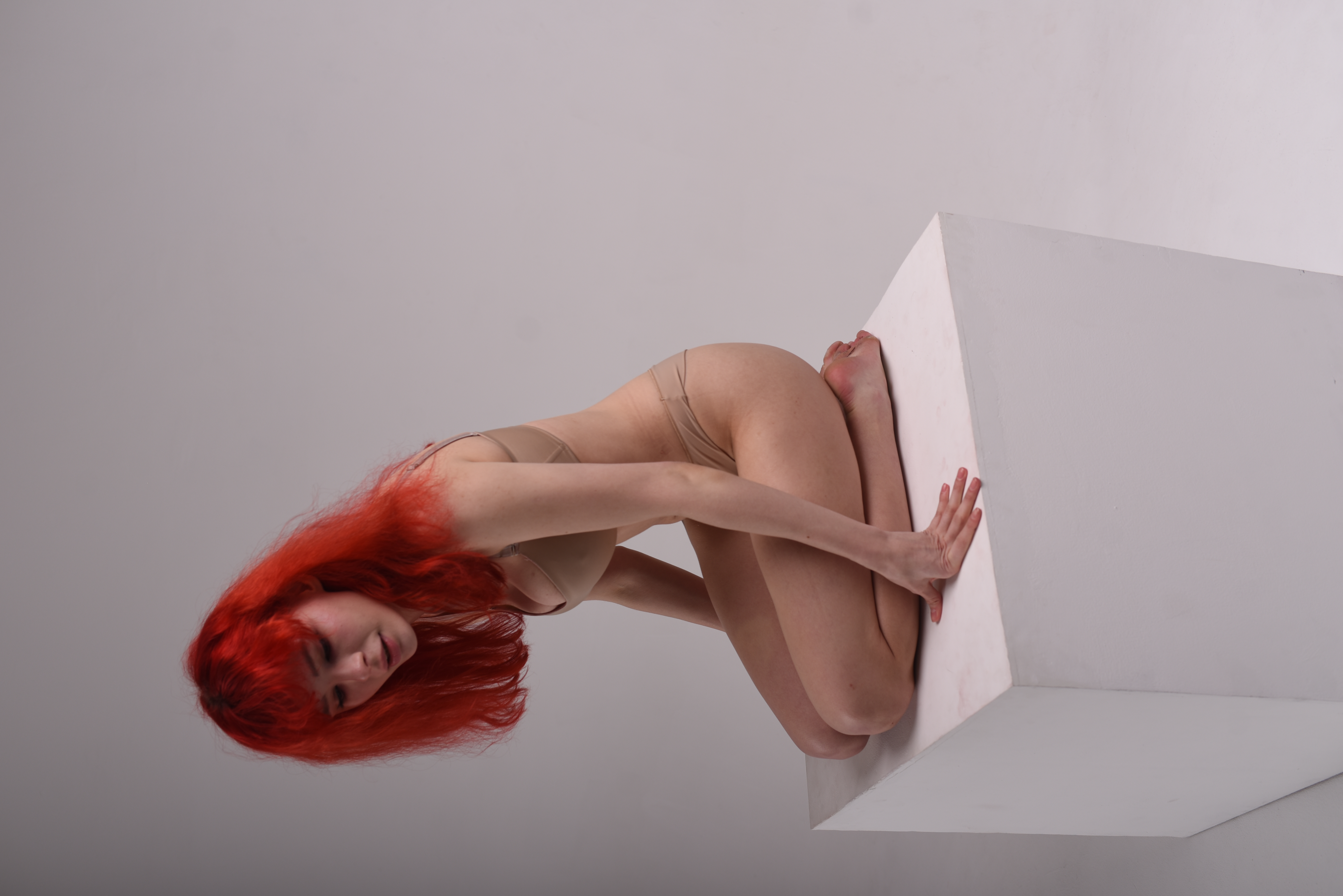 a woman with vibrant red hair is kneeling on a white cube in