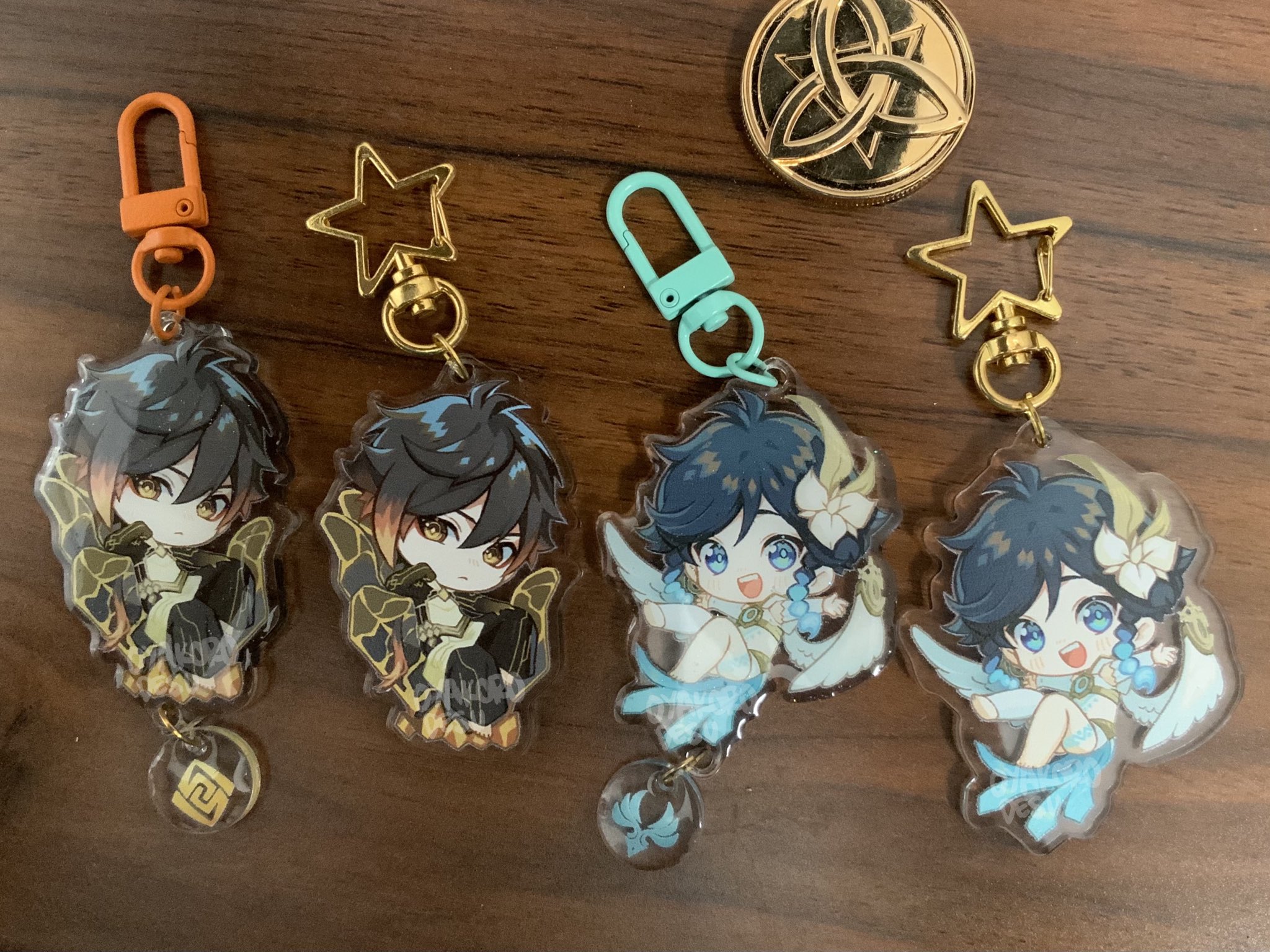 a close up image of four anime character keychains. they are all chibi style and have clear acrylic bodies with colorful artwork. two keychains are of  characters with dark hair and wings,  and the other two are of characters with light hair and wings. they all have a unique charm on the bottom.  the characters are  from the game genshin impact.