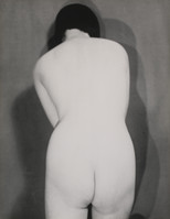 the image is a black and white photograph of a nude woman from behind.  she is positioned slightly hunched over, her back to the camera. her dark hair is pulled back, and the lighting is soft and diffused, casting a subtle shadow on the wall behind her. the overall aesthetic is minimalist and somewhat sensual, emphasizing the curves and form of the woman's body.  the style suggests a vintage or classic photographic approach.