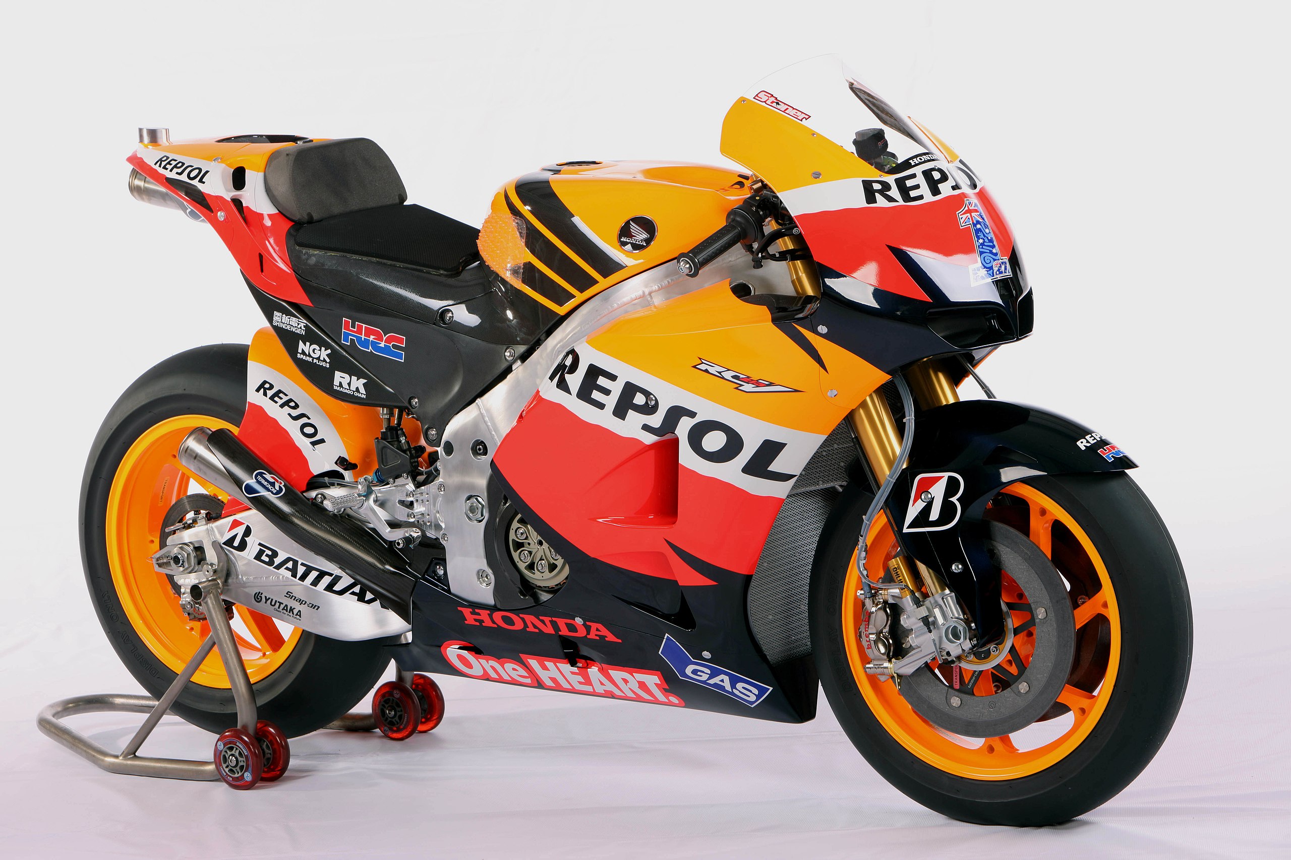 a closeup shot of a honda rc213v motogp motorcycle, livery sponsored by repsol, showcasing the detailed paintwork and branding. the motorcycle is on a stand with its front tire facing the camera, displaying its distinctive orange and black livery.