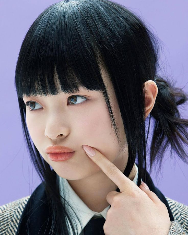 a young asian woman poses for a headshot wearing a black and white patterned jacket and a black tie. she has dark black hair with bangs and is looking at the camera with a slight smile.