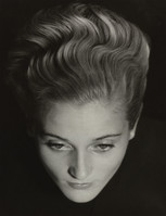 the image is a closeup black and white portrait of a woman's face and head.  her hair is styled in a dramatic, wavy updo characteristic of the 1930s. the style is meticulously crafted, with each wave clearly defined. her expression is serious and thoughtful, her eyes directly engaging the viewer. the lighting is dramatic, creating strong shadows and highlighting the texture of her hair and the contours of her face. the background is dark and unblemished, focusing all attention on the subject. the overall tone is one of classic elegance and sophistication. the photograph has the aesthetic quality of a vintage studio portrait, possibly from the 1930s or 1940s.