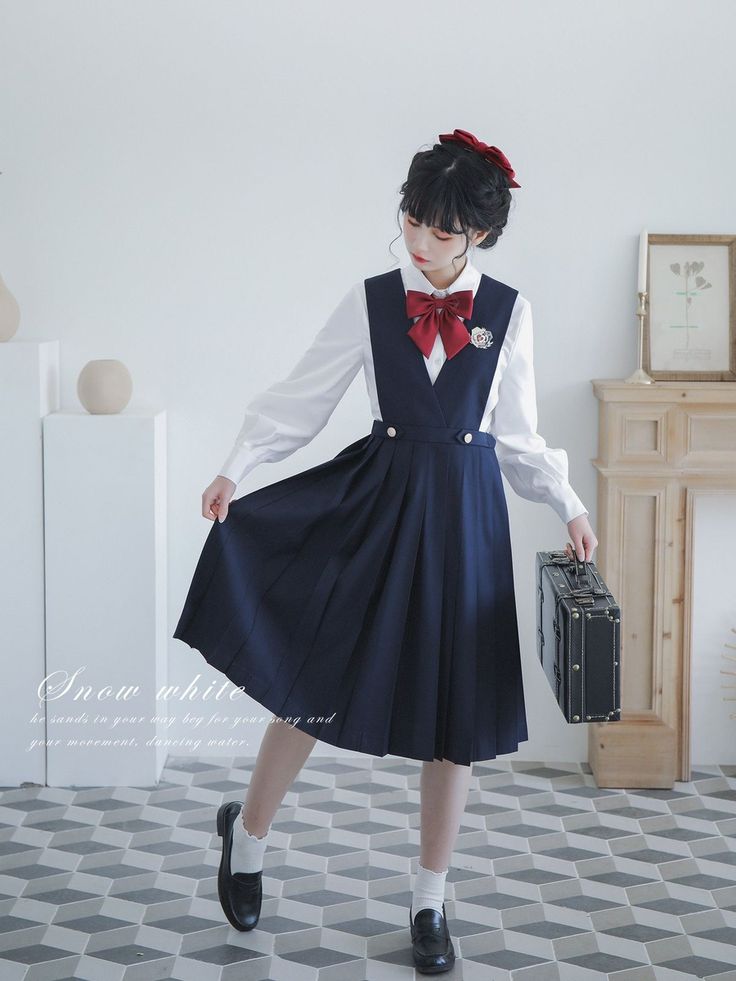 a woman is standing indoors, wearing a white shirt with a red bow, a navy pleated skirt, white socks, and black loafers. she is holding a briefcase in her right hand. she has a red bow in her hair. the skirt is part of a school uniformstyle dress.