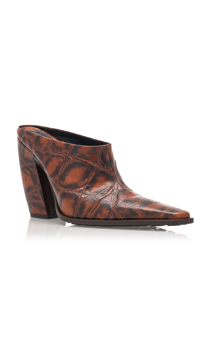a pair of brown leather mules with a crocodile embossed texture. the shoes have a high block heel and a pointed toe. they are styled in a western fashion. the shoes are shown against a white background.