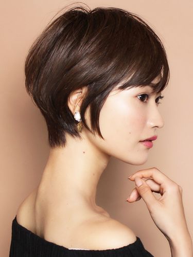 a young asian woman with short, styled hair, wearing a simple black top, looks at the camera with a slight smile while posing for a studio photo.  her makeup is light and clean and her skin is flawless.  she is wearing simple, pearl earrings.