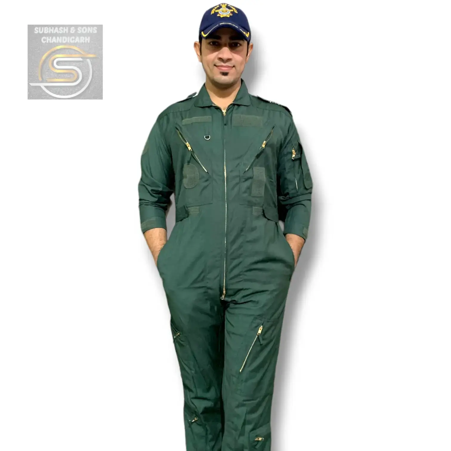 a man wearing a green flight suit with a navy blue cap with an insignia on top. he is standing with his hands in his pockets.